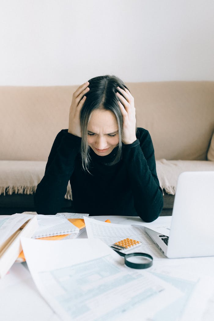 A woman appears stressed and overwhelmed with paperwork at her home desk.